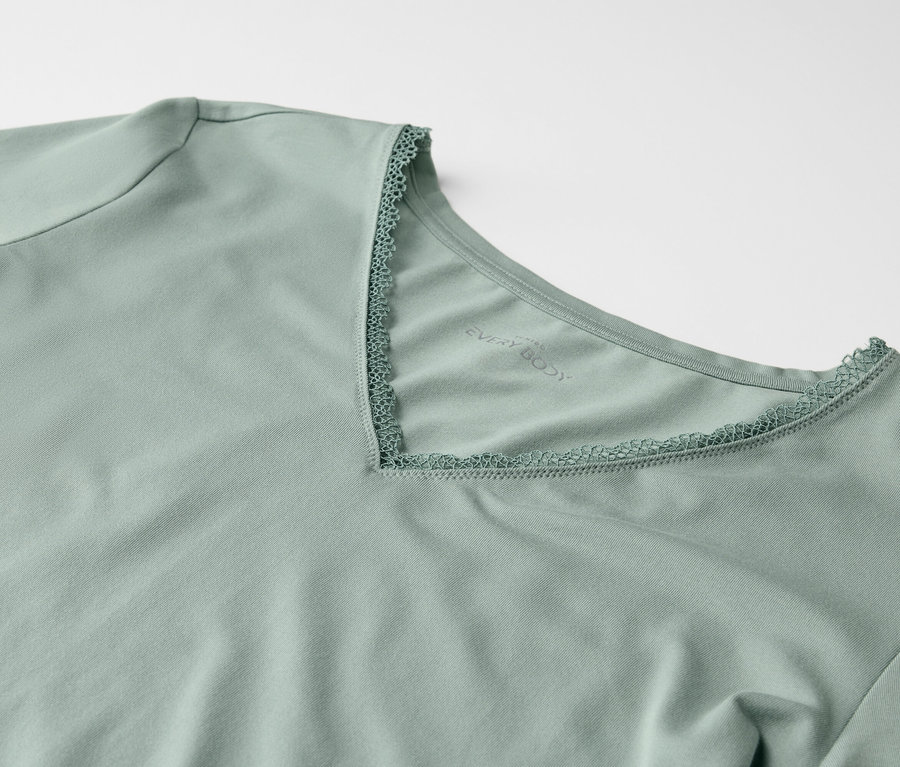 Detail svetlozeleného trička s krátkym rukávom a výstrihom do V lemovaným čipkou.