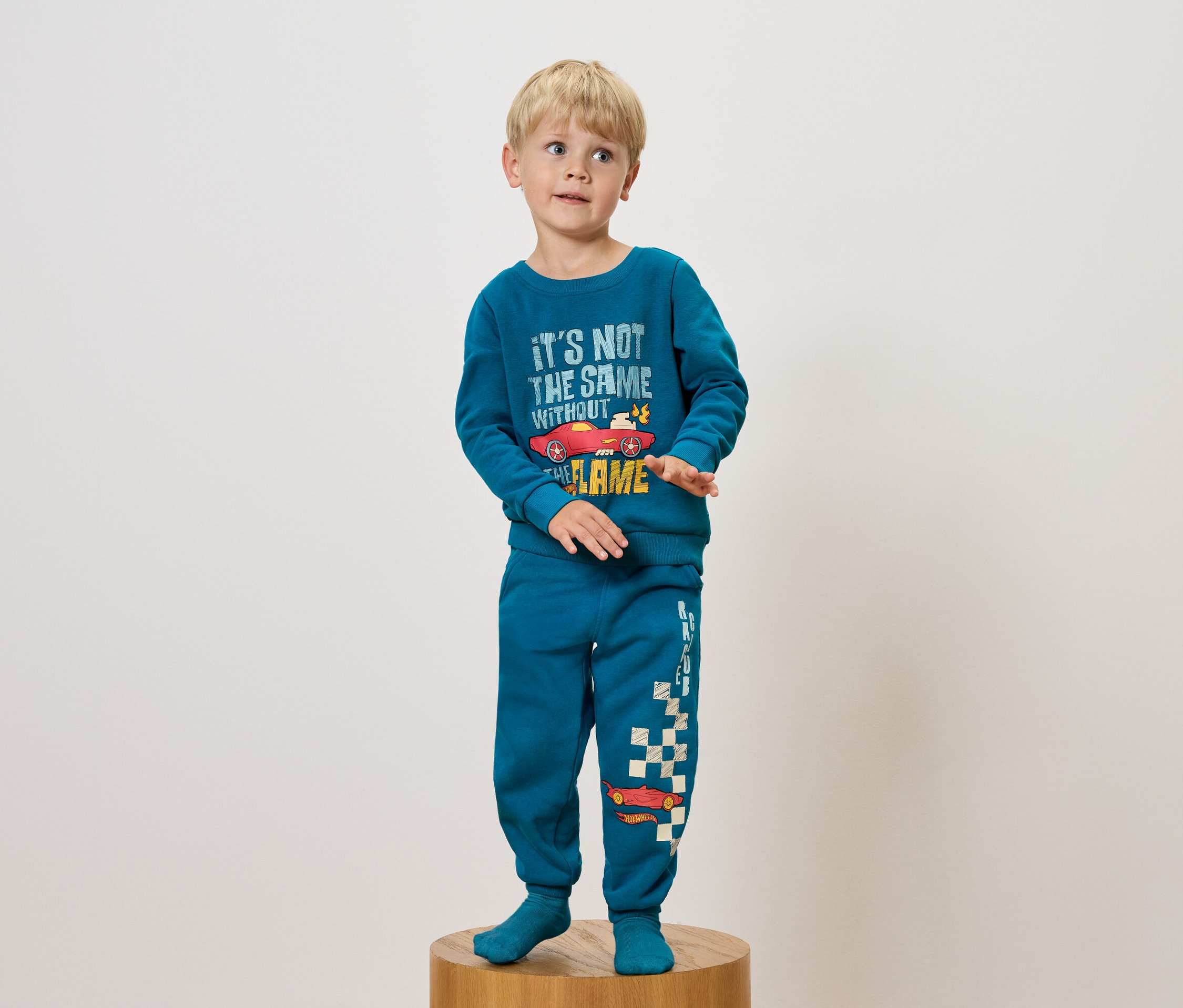 Chlapec v modrom pyžame s potlačou auta stojí na drevenom podstavci.