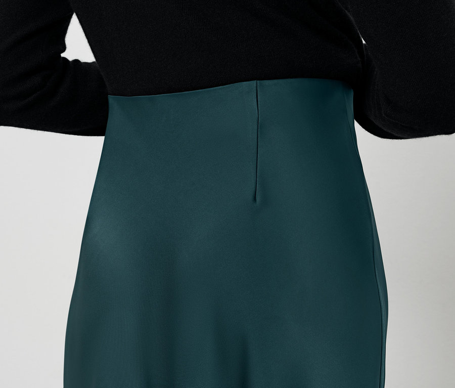 Pohľad zozadu na ženu v čiernej blúzke a zelenej sukni.