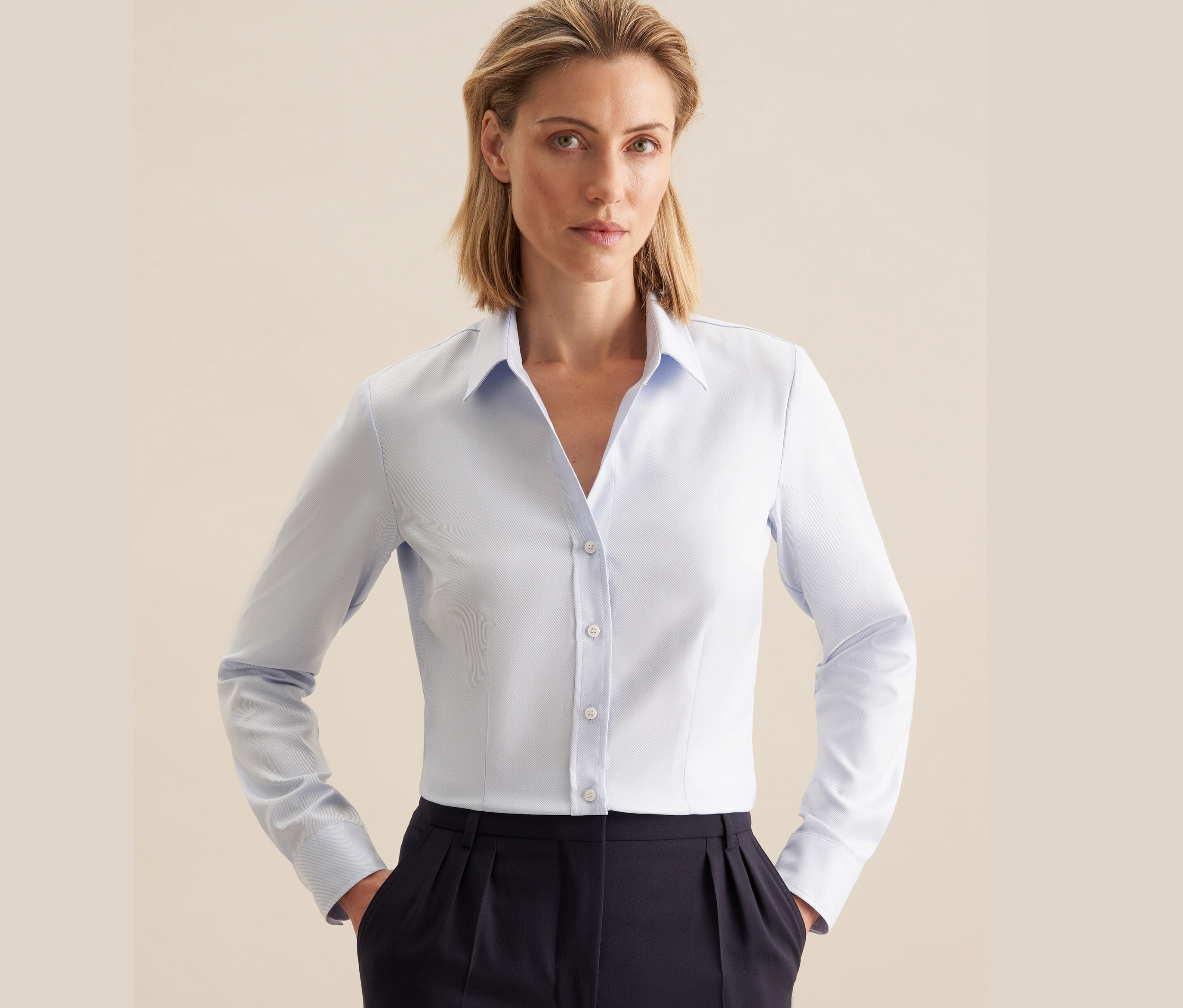 Žena má na sebe svetlomodrú keprovú blúzku Seidensticker a tmavomodré nohavice.