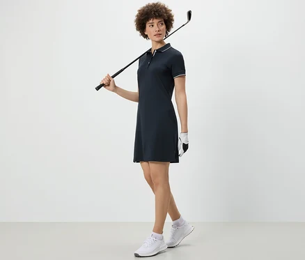 Žena drží golfovú palicu cez rameno a má na sebe športové šaty.