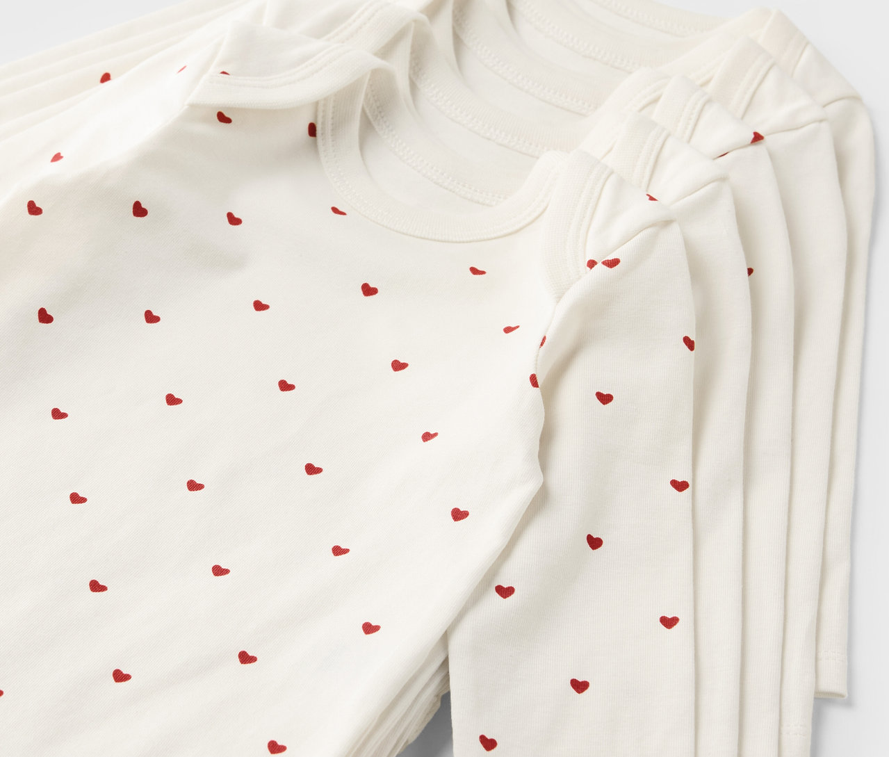 Hromada piatich bielych dojčenských body s rastúcou funkciou a červeným vzorom srdca.