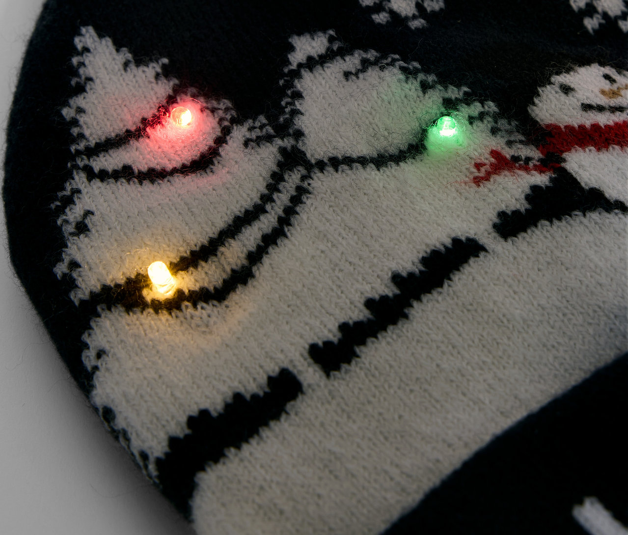 Detail čierno-bielej pletenej čiapky so snehovými vločkami a snehuliakmi, zdobené farebnými svetlami.
