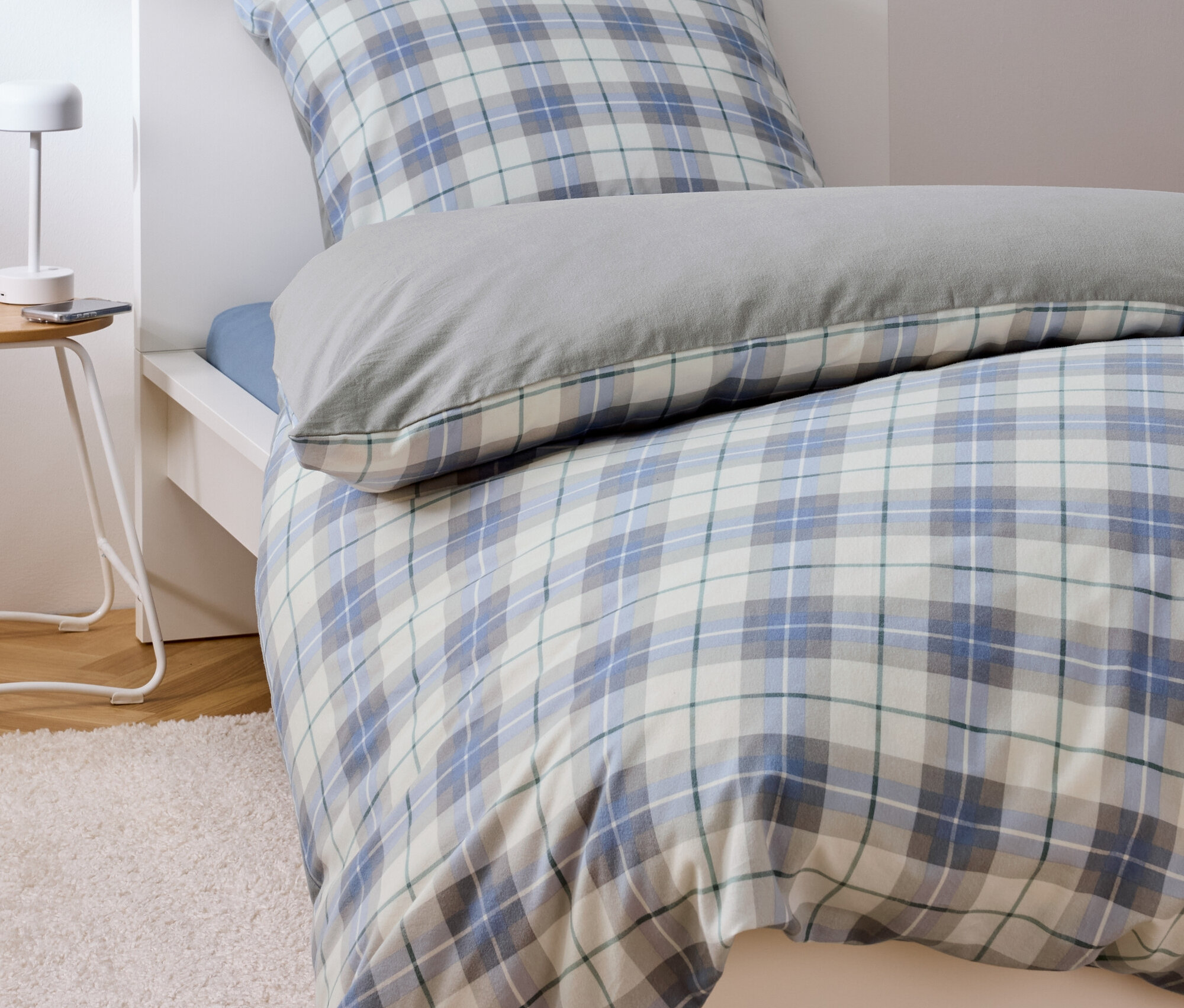 Posteľ s modro-bielou kockovanou posteľnou bielizňou a sivým vankúšom.