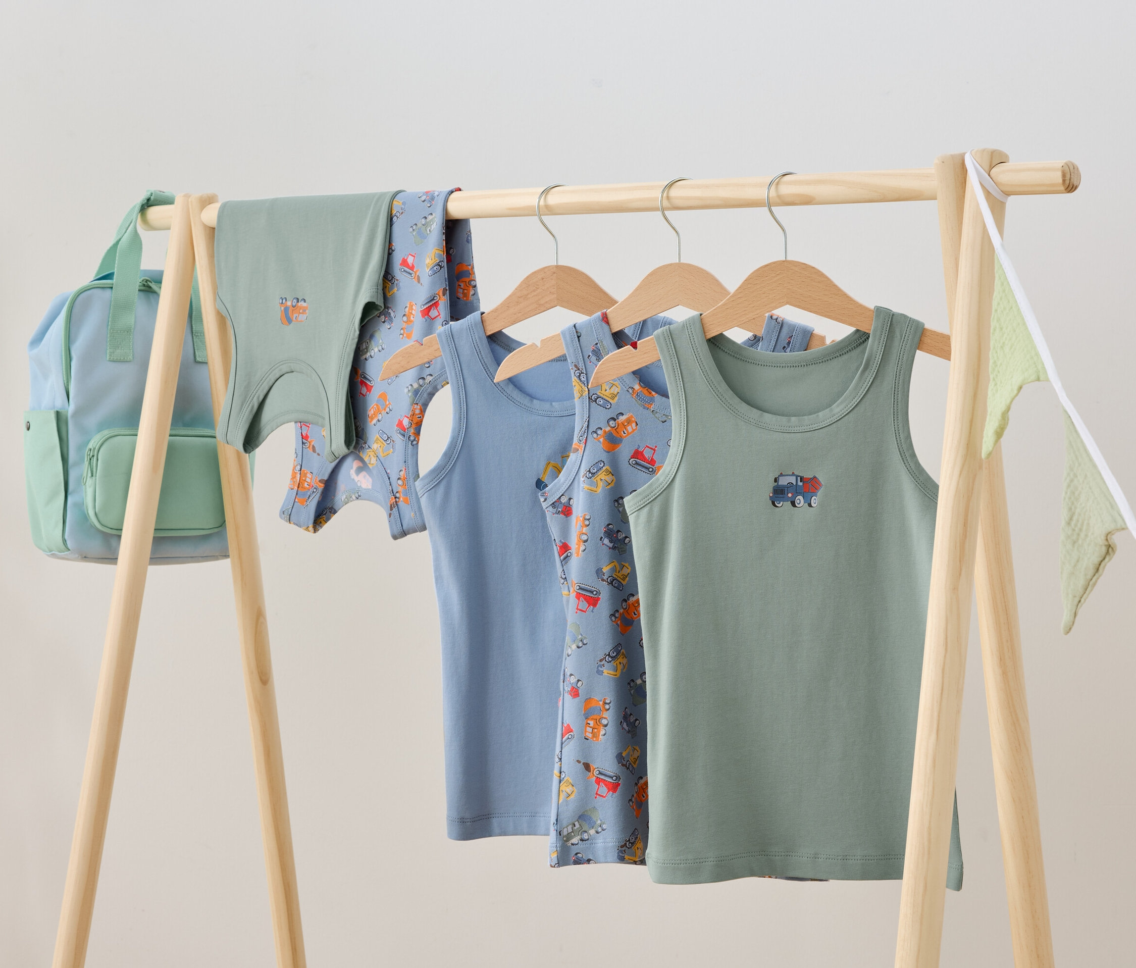 Detské oblečenie visí na drevenom stojane, vrátane tielok a batohu.