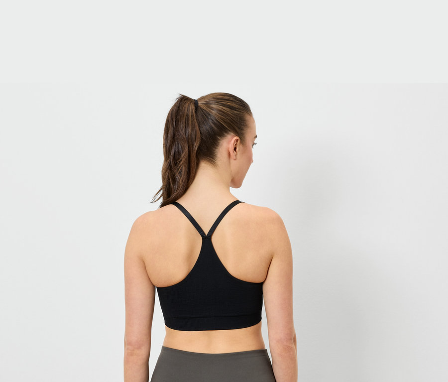 Pohľad zozadu na ženu s copom v čiernej športovej podprsenke a sivých legínach.