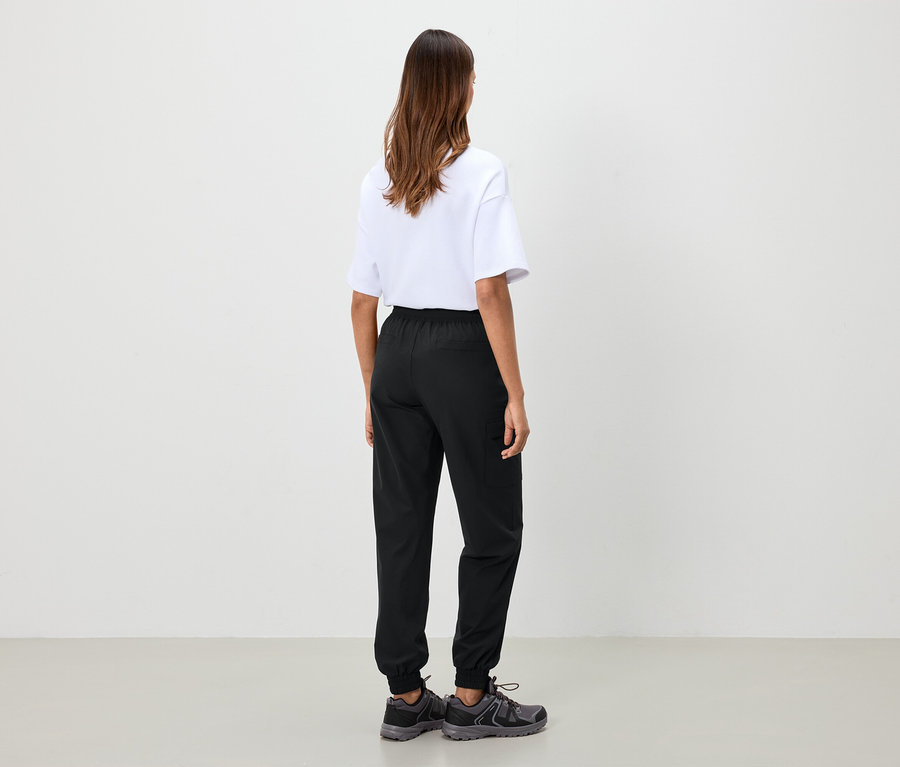 Žena stojí chrbtom a má na sebe biele tričko, čierne nohavice a sivé topánky.