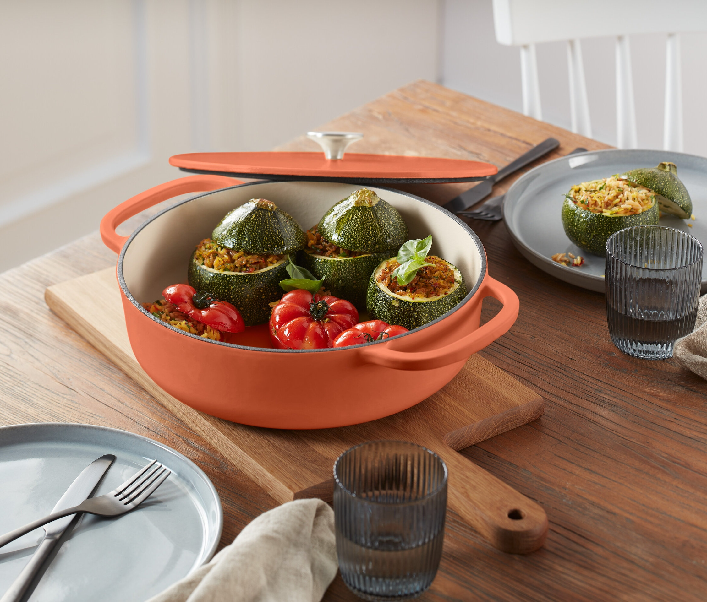 Plnené cukety a paradajky v oranžovom hrnci na drevenej doske.