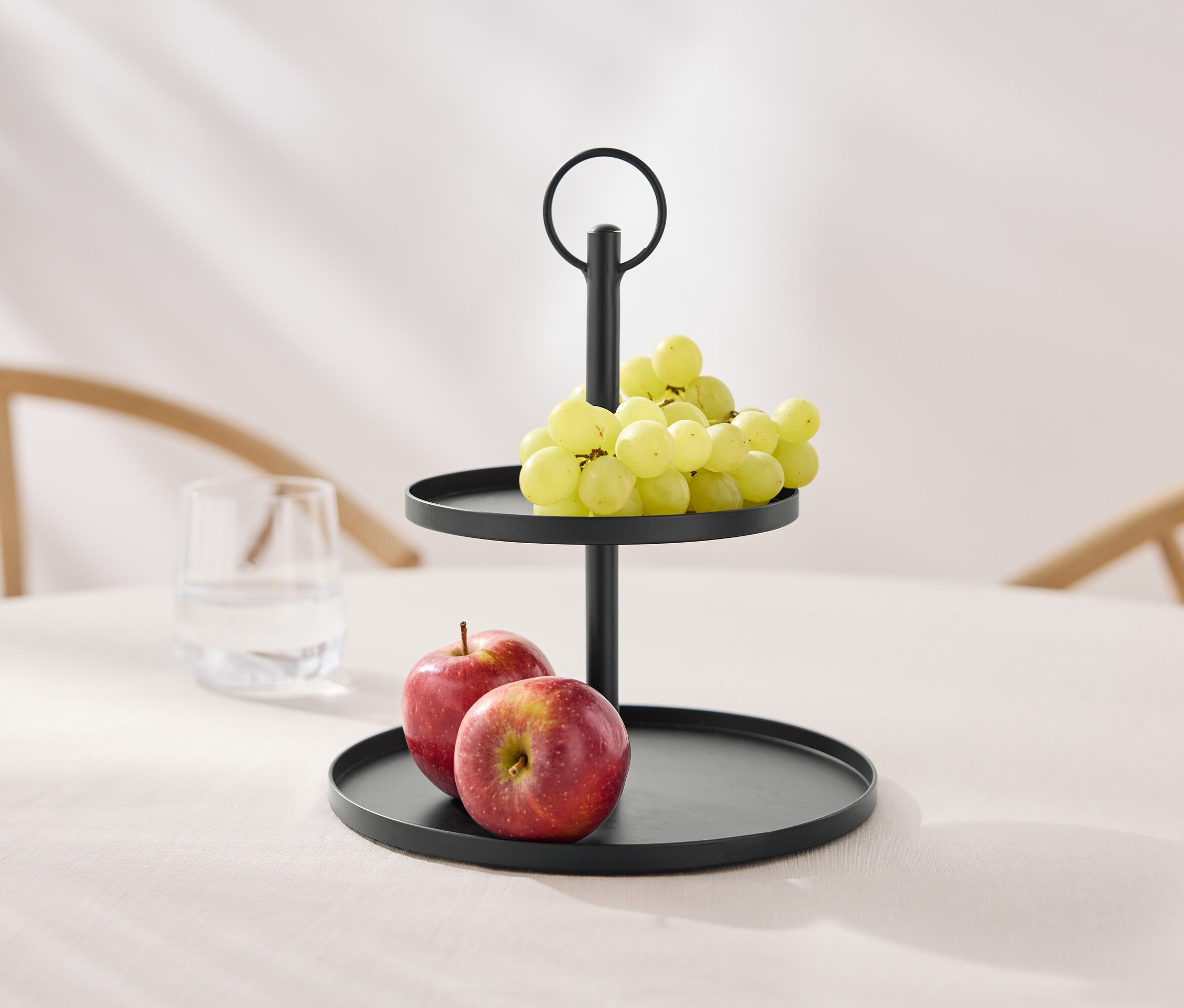 Dvojposchodová čierna etažér s hroznom a jablkami na stole.