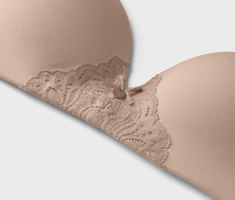 Detailný záber béžovej podprsenky s čipkovaným lemom a malým ozdobným gombíkom.