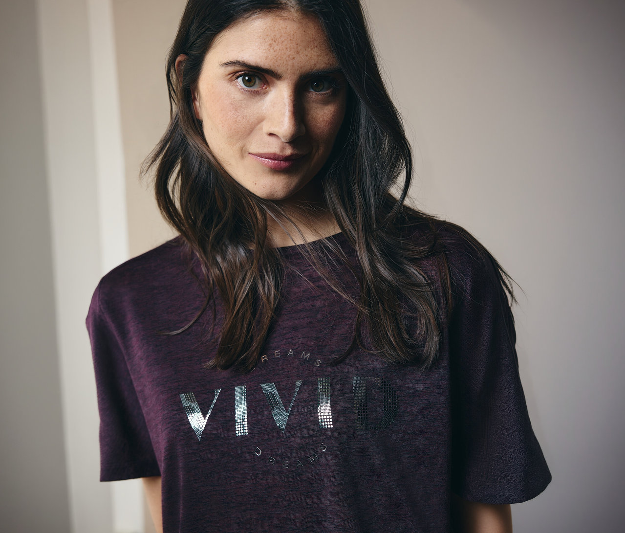 Žena s dlhými hnedými vlasmi má na sebe gaštanové tričko s nápisom "Vivid Dreams".