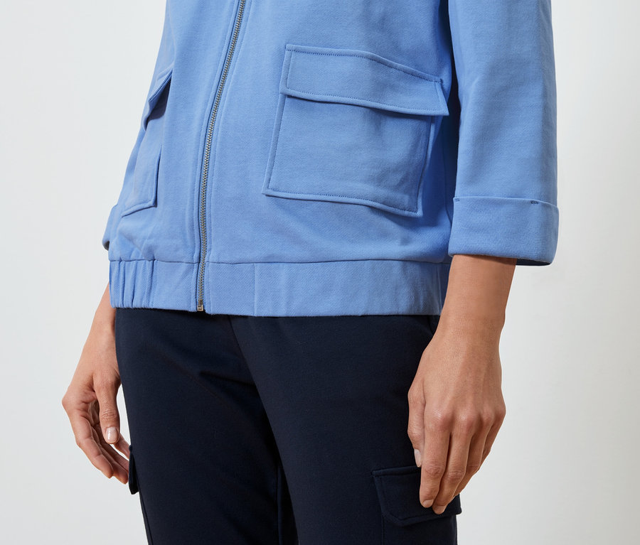 Žena má na sebe svetlomodrú bundu a tmavomodré nohavice.