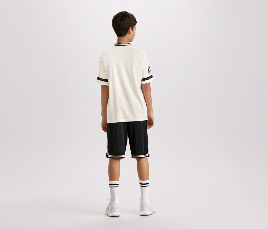 Pohľad zozadu na mladého muža v krémovom tričku s krátkym rukávom s čiernymi pruhmi na golieri a rukávoch, čiernych šortkách s bielymi pruhmi a bielych ponožkách a topánkach.
