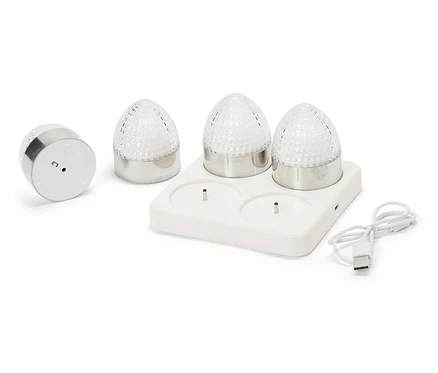 Štyri malé okrúhle lampy so striebornými základňami a fasetovanými, priehľadnými sklenenými kupolami stoja na bielej nabíjacej stanici s USB káblom.