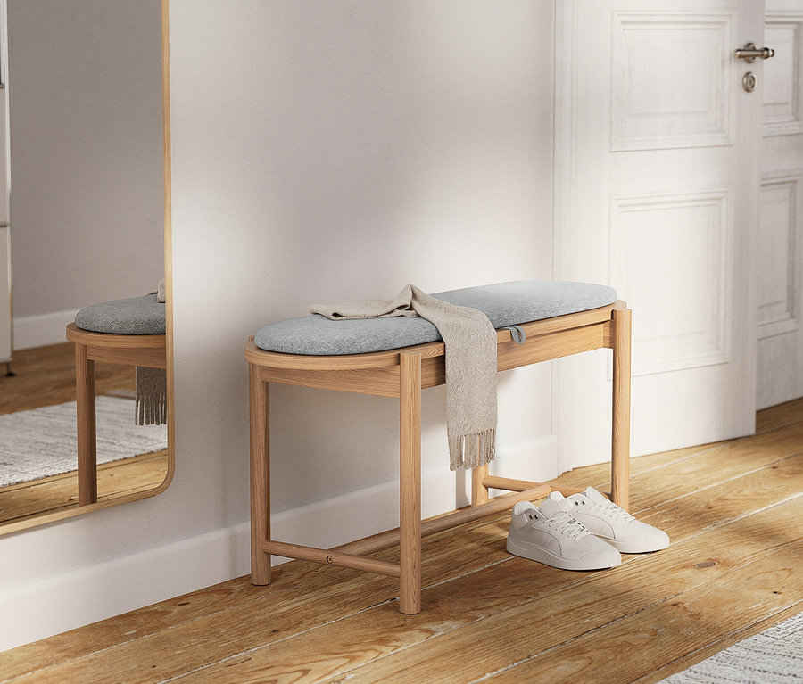 Svetlá drevená lavica so svetlomodrým vankúšom a béžovým šálom. Pod ním sú biele tenisky.