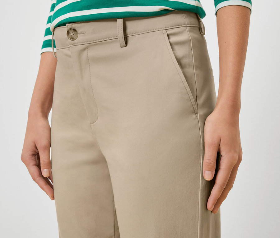 Detailný záber ženy v béžových nohaviciach a zeleno-bielom pruhovanom tope.