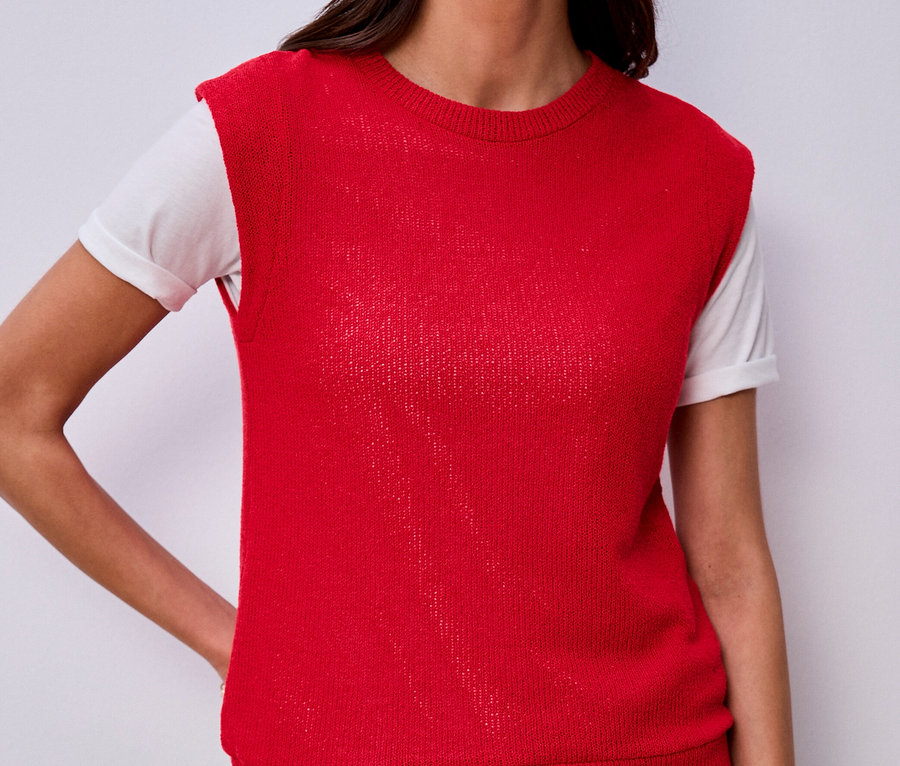 Žena v tričku Street One pod červenou pletenou vestou a džínsami, s rukou vo vrecku.