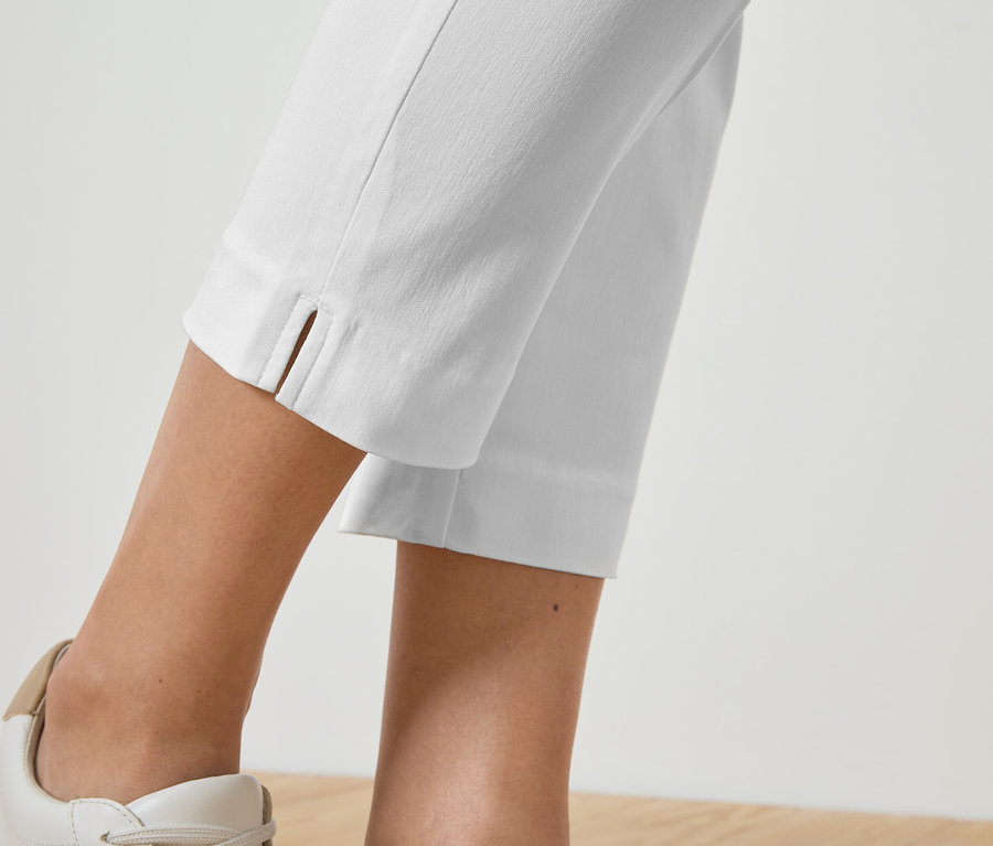 Detailný záber na nohy osoby v bielych nohaviciach a ladiacich teniskách.