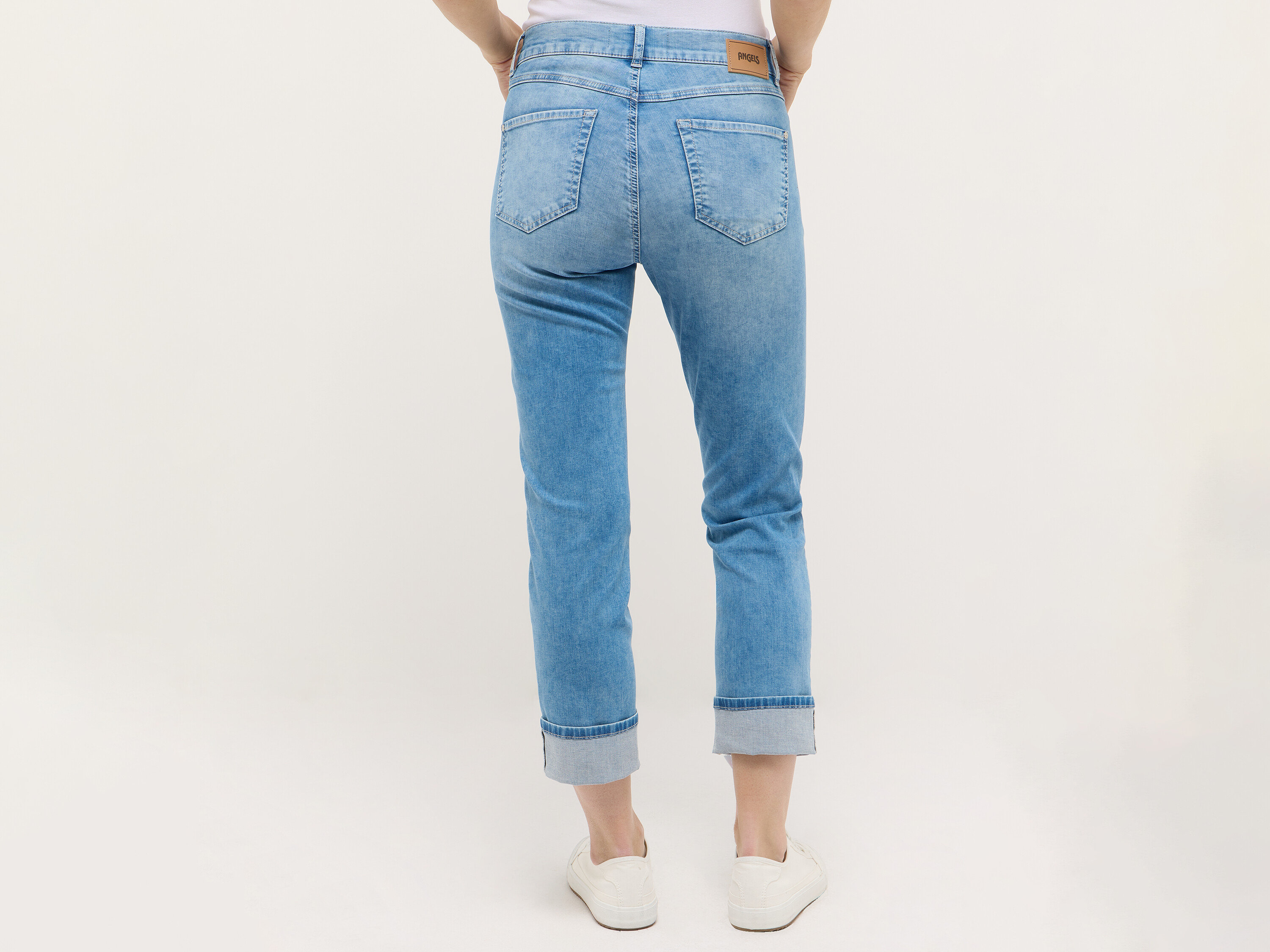 Boky a nohy ženy v svetlomodrých džínsoch a bielych teniskách, pohľad zozadu.