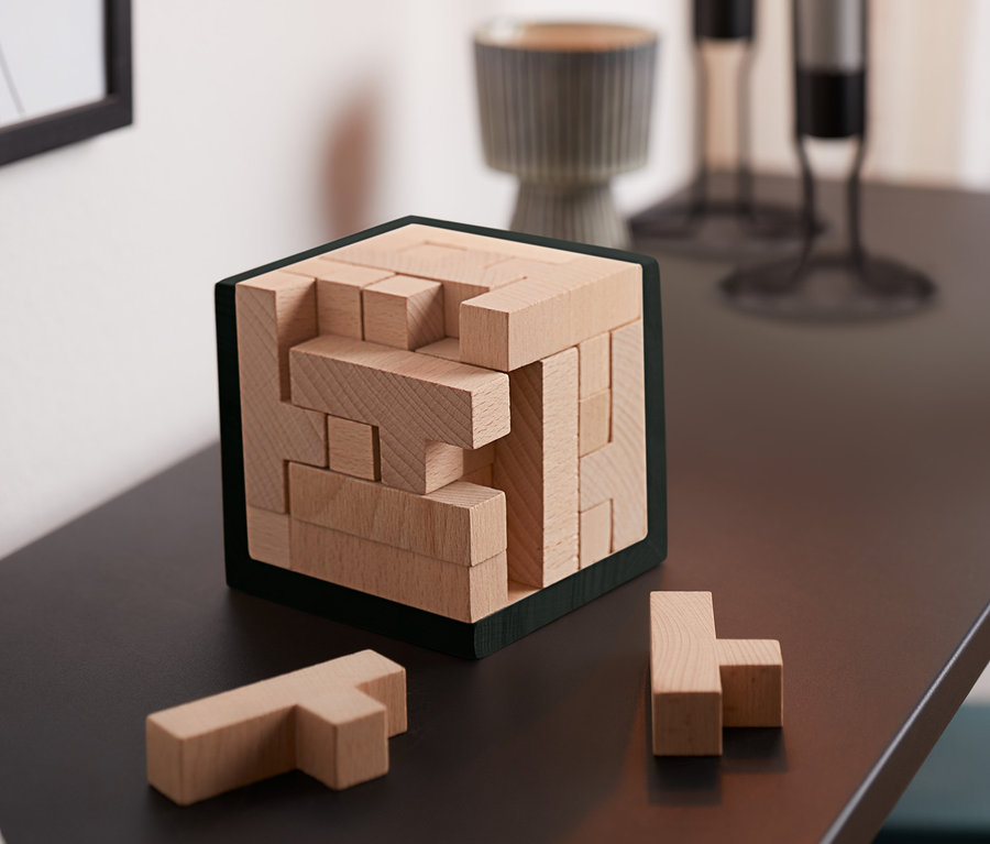 Na stole stojí IQ puzzle kocka a dva diely sú vedľa nej.