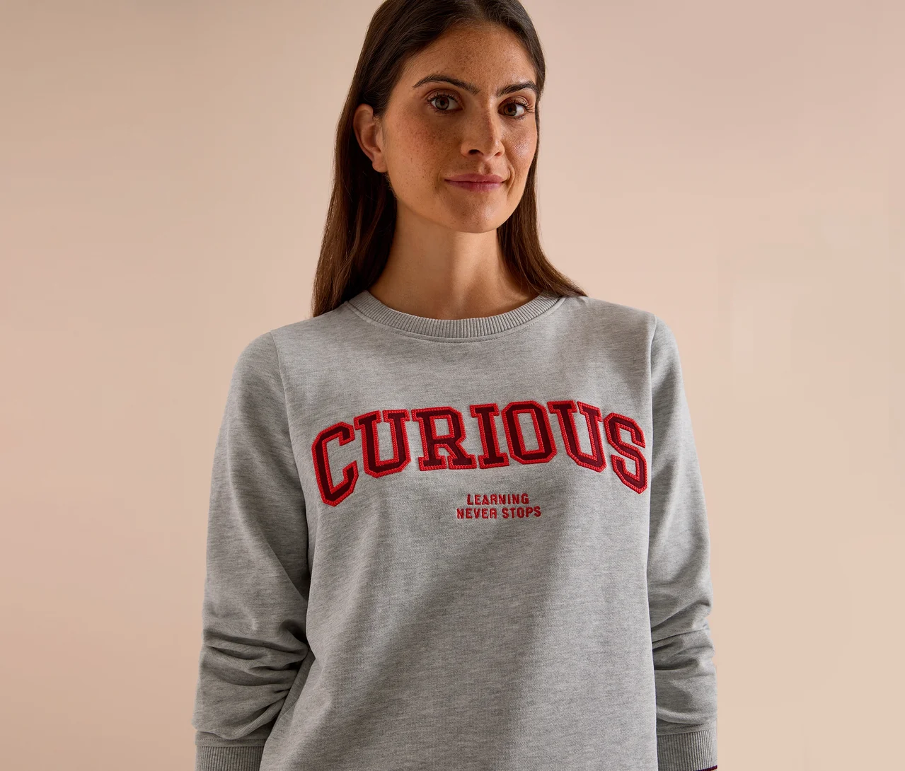 Žena má na sebe sivú mikinu CECIL s červeným nápisom "CURIOUS" a "LEARNING NEVER STOPS".