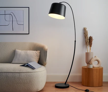 Čierna oblúková lampa z kovu stojí vedľa béžovej pohovky.