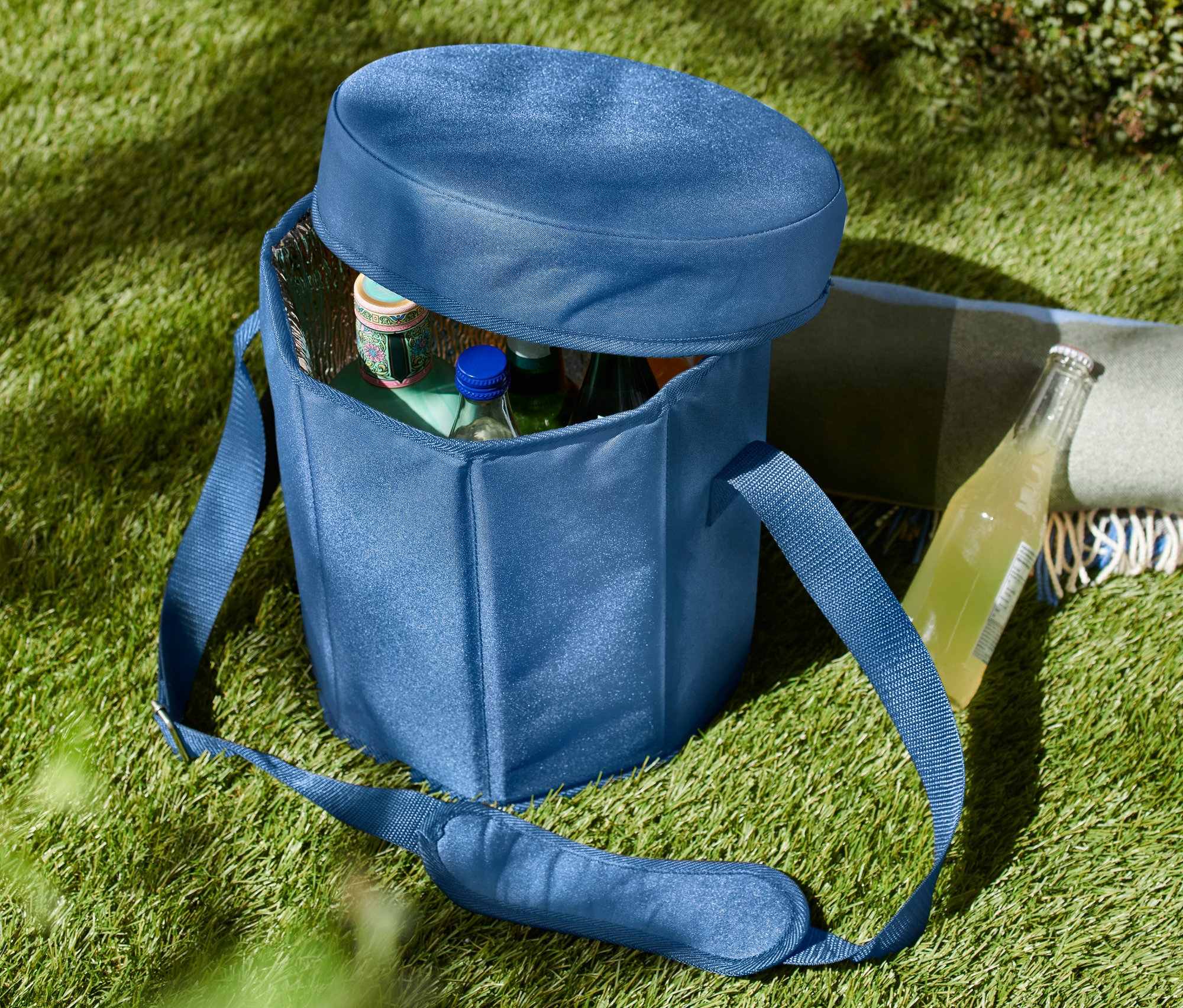 Modrá chladiaca taška 2 v 1 na tráve, čiastočne otvorená, s fľašami vnútri.