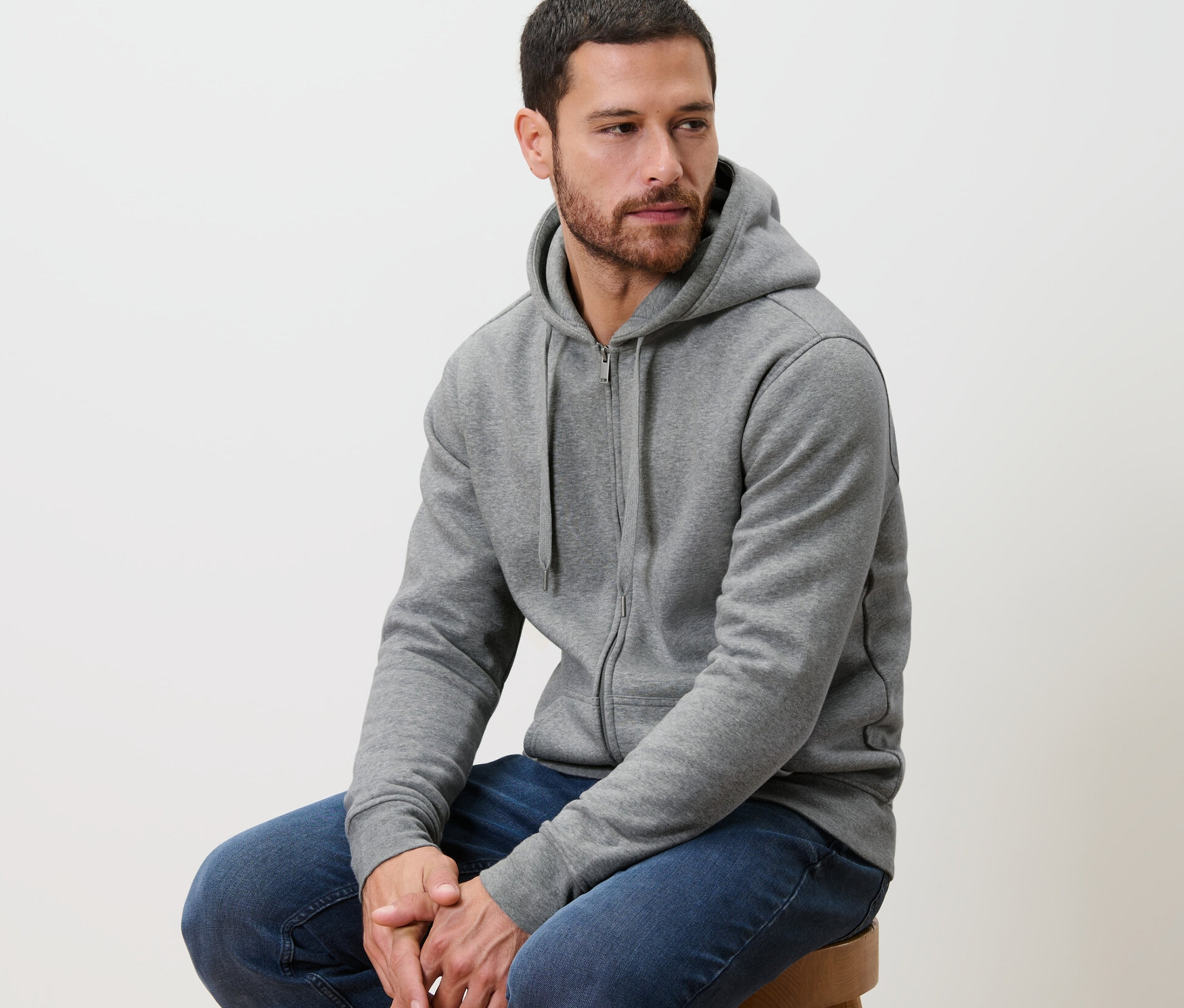 Muž sedí na stoličke a má na sebe sivú mikinu s kapucňou.