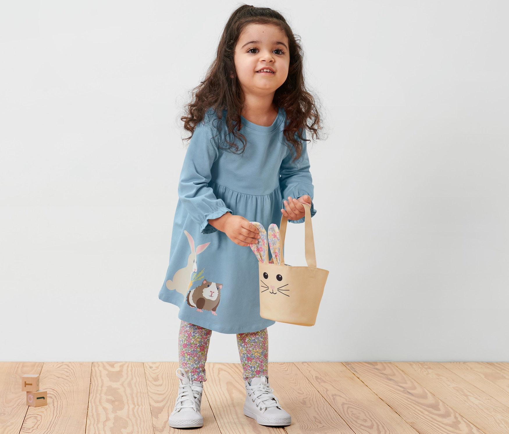 Dievčatko v detských džersejových šatách drží tašku s králičími ušami.