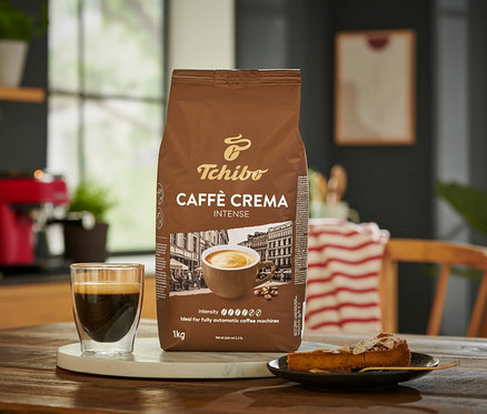 Balenie zrnkovej kávy Caffè Crema Intense 1 kg vedľa šálky kávy a kúska koláča.