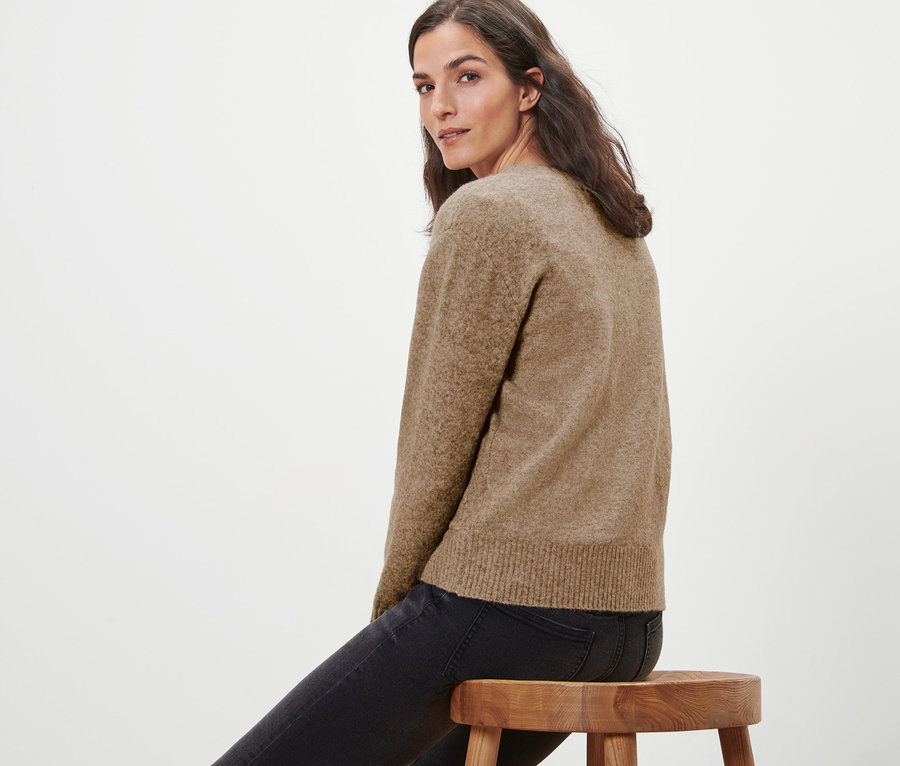 Žena sedí na drevenej stoličke a má na sebe pletený sveter s vlnou.