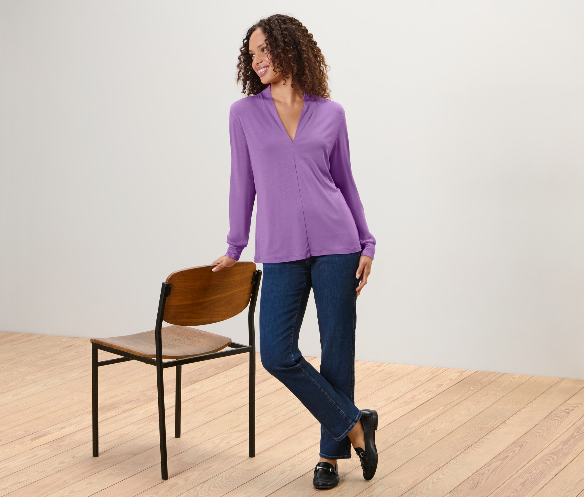 Žena pózuje v blúzkovom tričku s výstrihom do V, džínsoch a mokasínach.