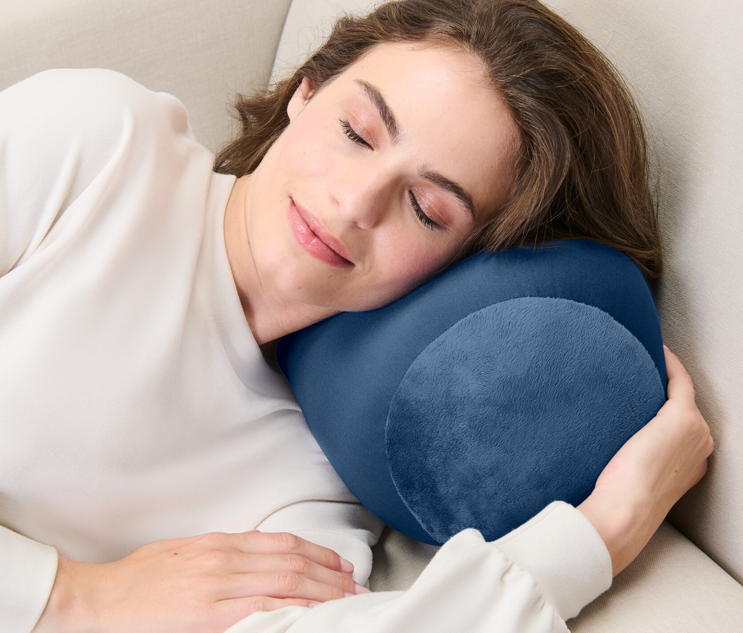 Žena spí na béžovej pohovke s relaxačným vankúšom.