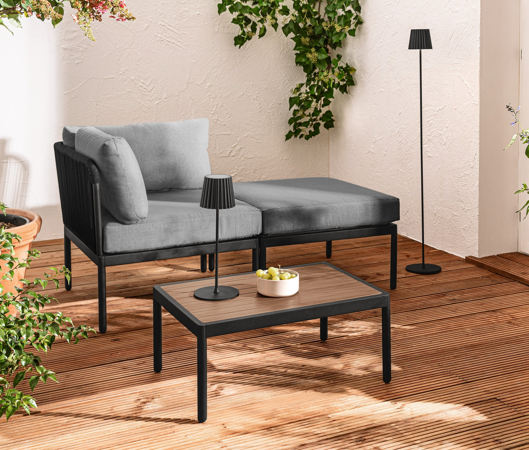 Terasa s modulárnym relaxačným nábytkom s textilným výpletom, čiernou LED akumulátorovou stolovou a stojacou lampou a LED filamentovou svetelnou reťazou.