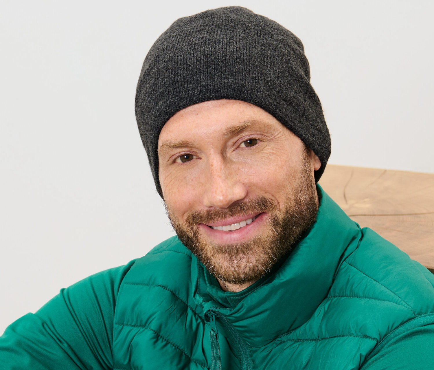 Muž s bradou sa usmieva, má na sebe pletenú čiapku a zelenú vestu.