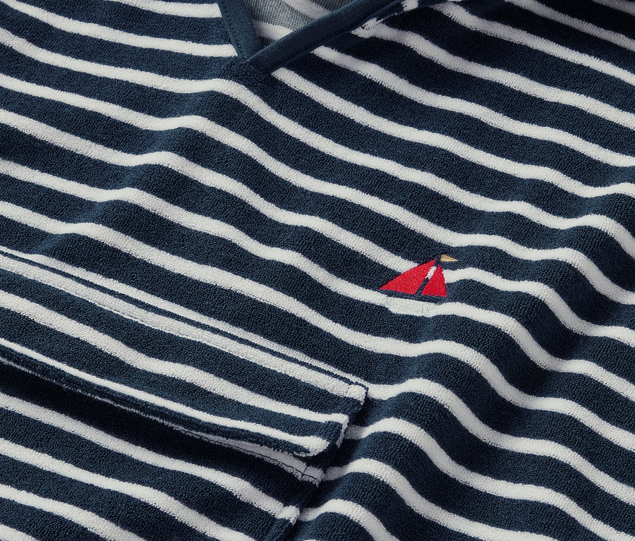 Detail froté ponča, pobrežie, s modro-bielymi pruhmi a malou červenou výšivkou plachetnice.