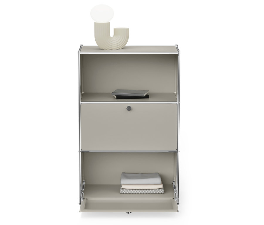 Sivá skrinka so strieborným rámom má otvorenú spodnú policu so zloženým oblečením a hornú policu s knihami.