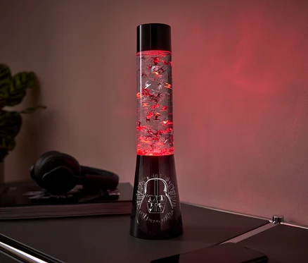 Čierna lávová lampa s motívom Darth Vadera na podstavci a červenými trblietkami vo vnútri stojí na stole.