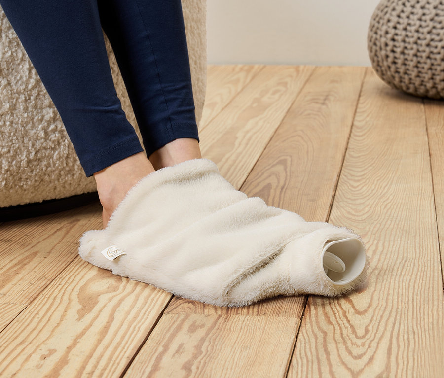 Nohy v modrých legínach vložené do chlpatého, krémovo sfarbeného návleku na horúcu fľašu.