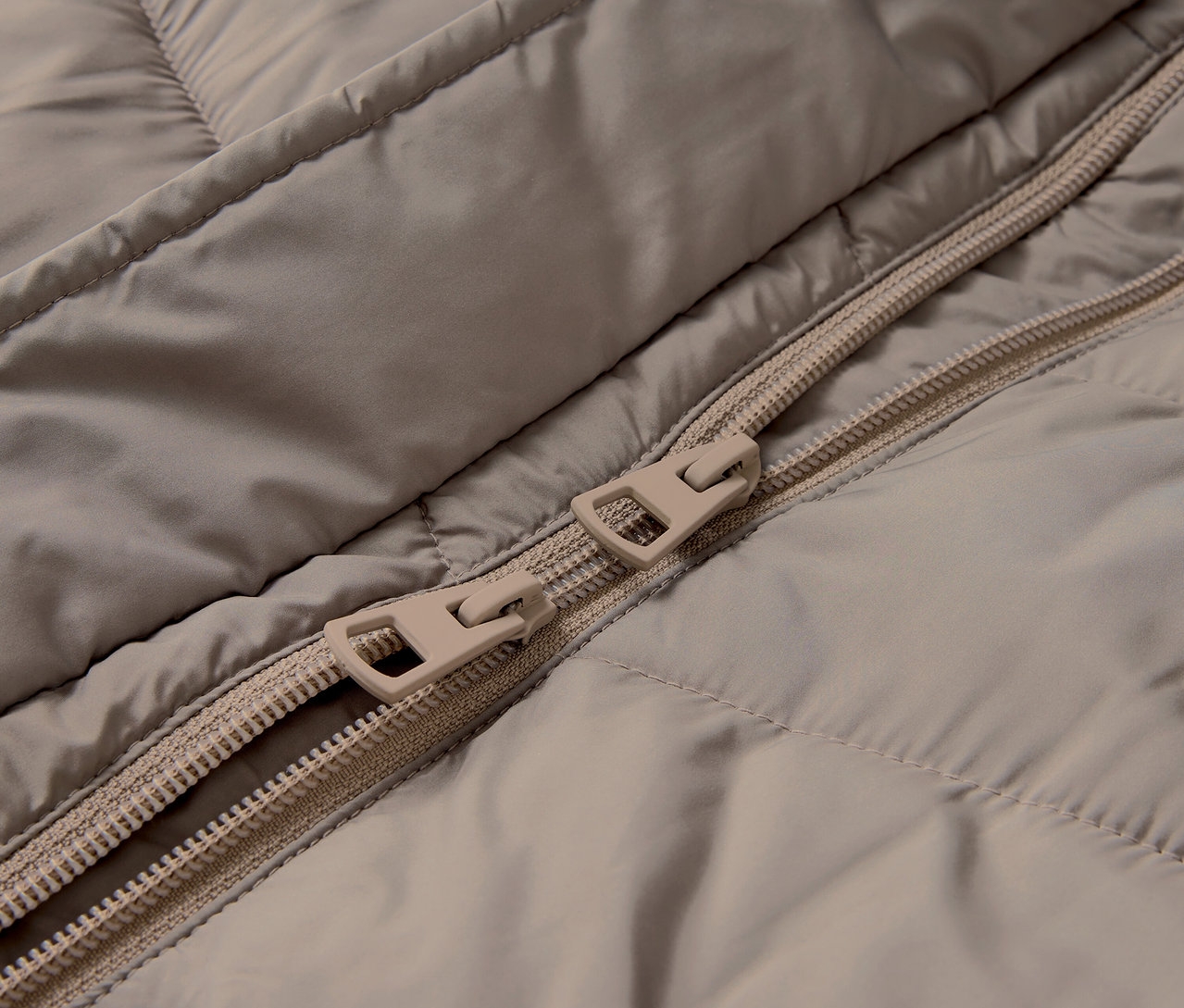 Detail béžovej prešívanej bundy so zipsom.