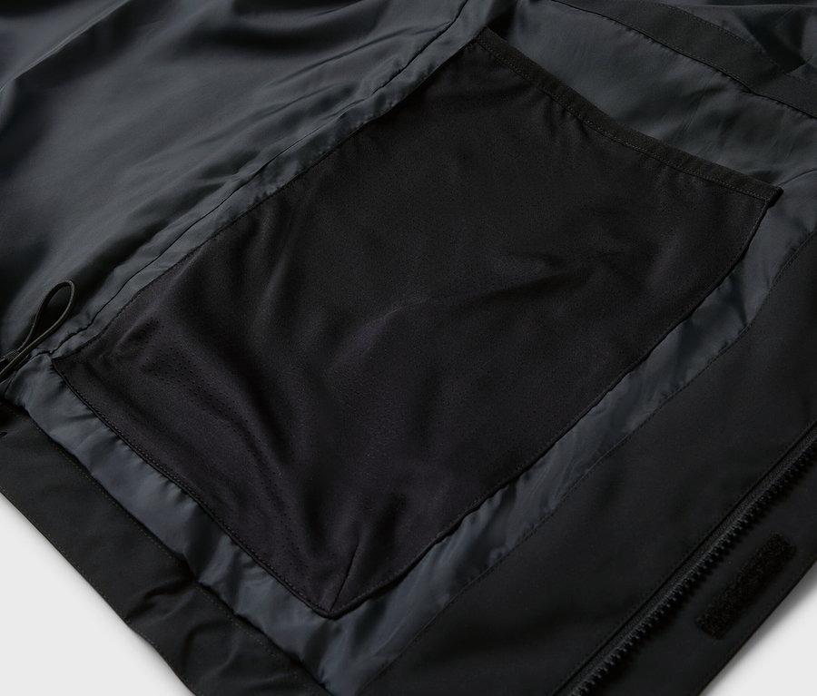 Detail čiernej bundy s vreckom na zips.