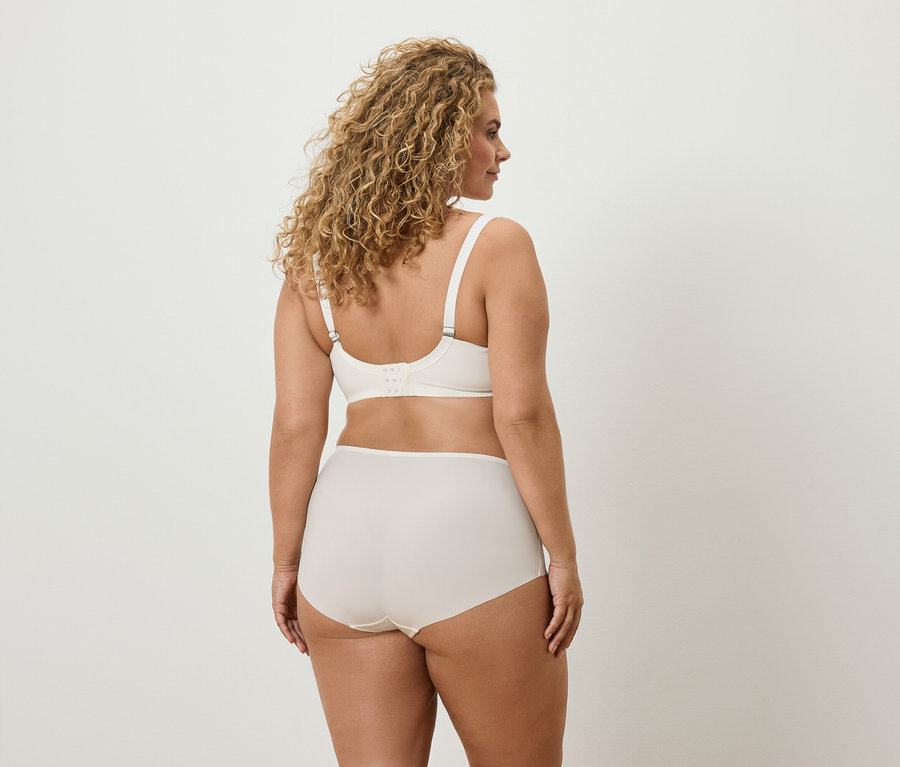 Zozadu: žena s kučeravými vlasmi má na sebe krémovú podprsenku a nohavičky.