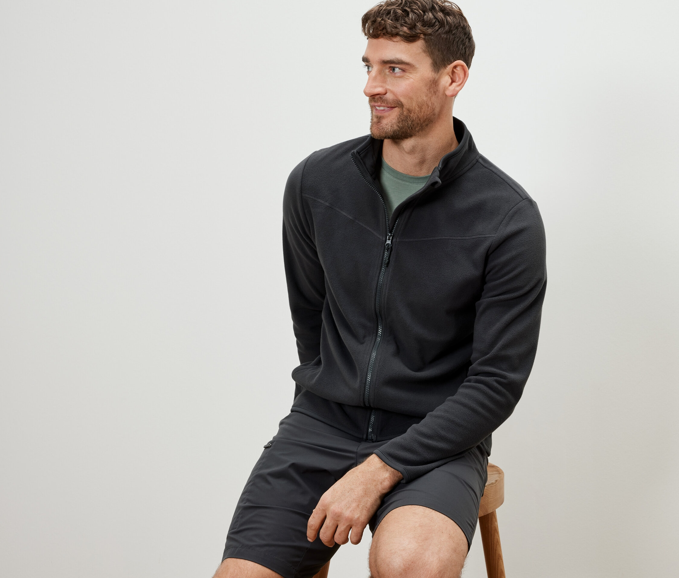 Muž sedí na stoličke a má na sebe antracitovú flísovú mikinu.