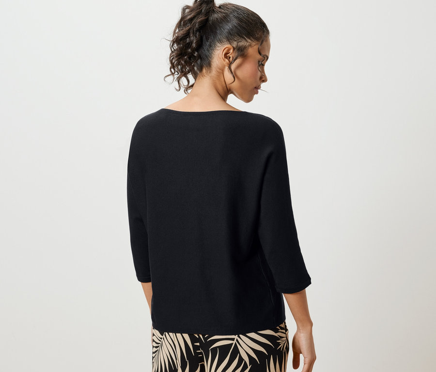 Žena chrbtom k fotoaparátu má na sebe čierny pulóver z jemného úpletu.