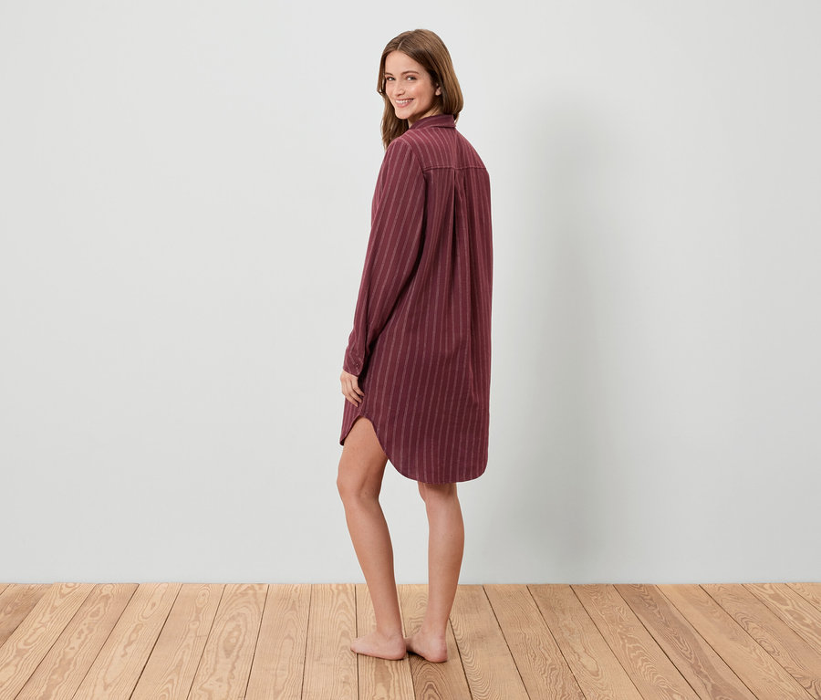 Žena sa pozerá cez plece a pózuje v pruhovanej košeľovej nočnej košeli.