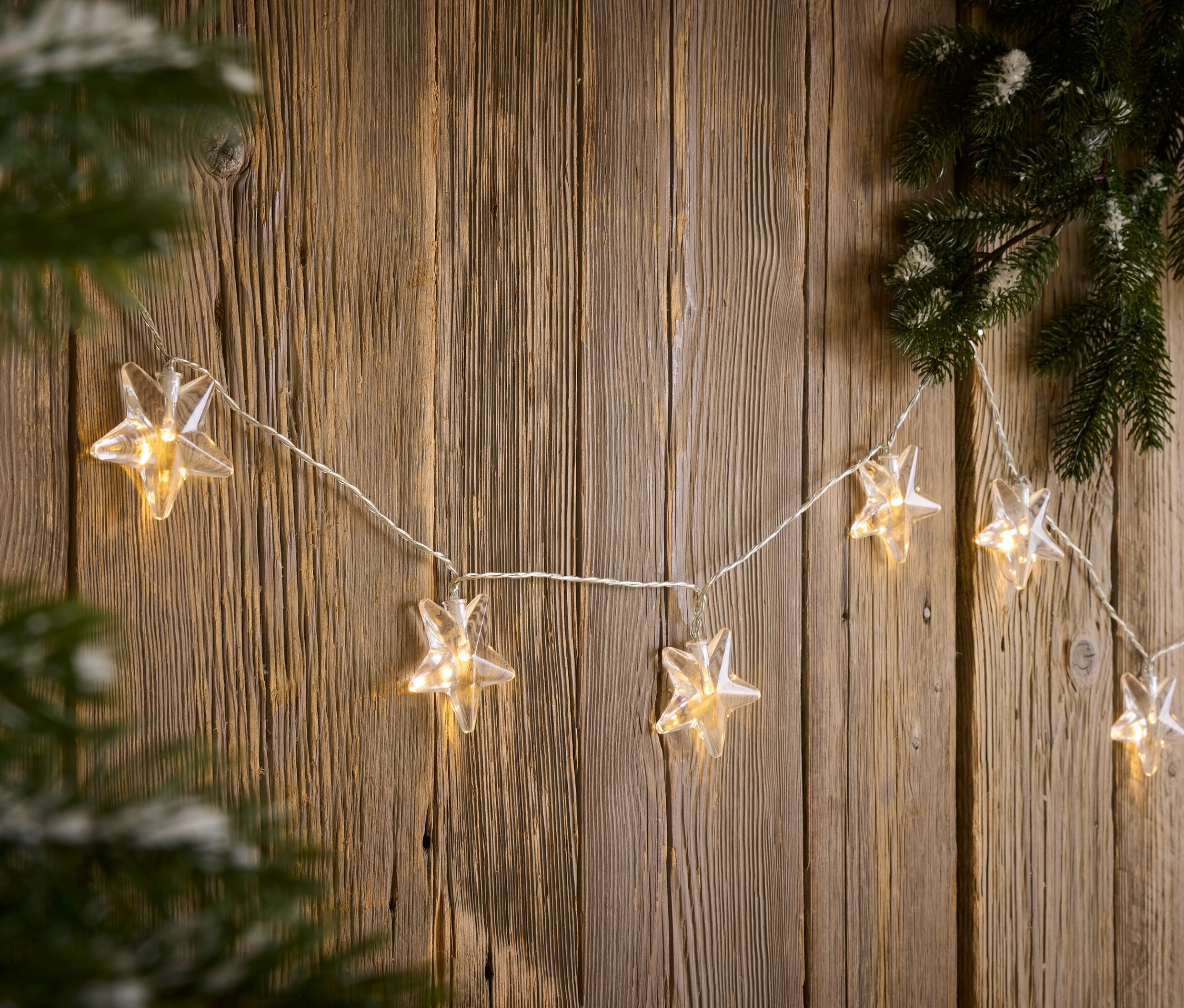 Reťaz svetiel v tvare hviezdy visí na drevenej stene vedľa borovicovej vetvy.