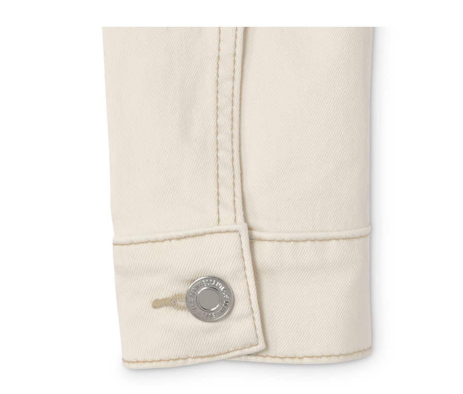 Detail krémovobielej džínsovej bundy s gombíkom.