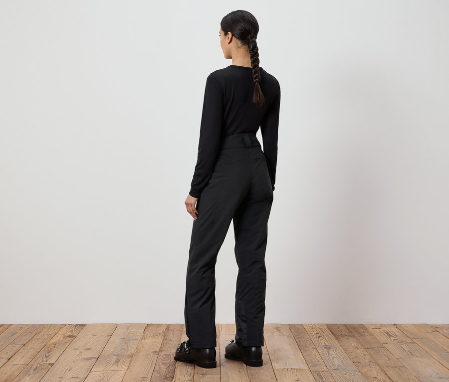 Žena v čiernom svetri a nohaviciach stojí chrbtom ku kamere.