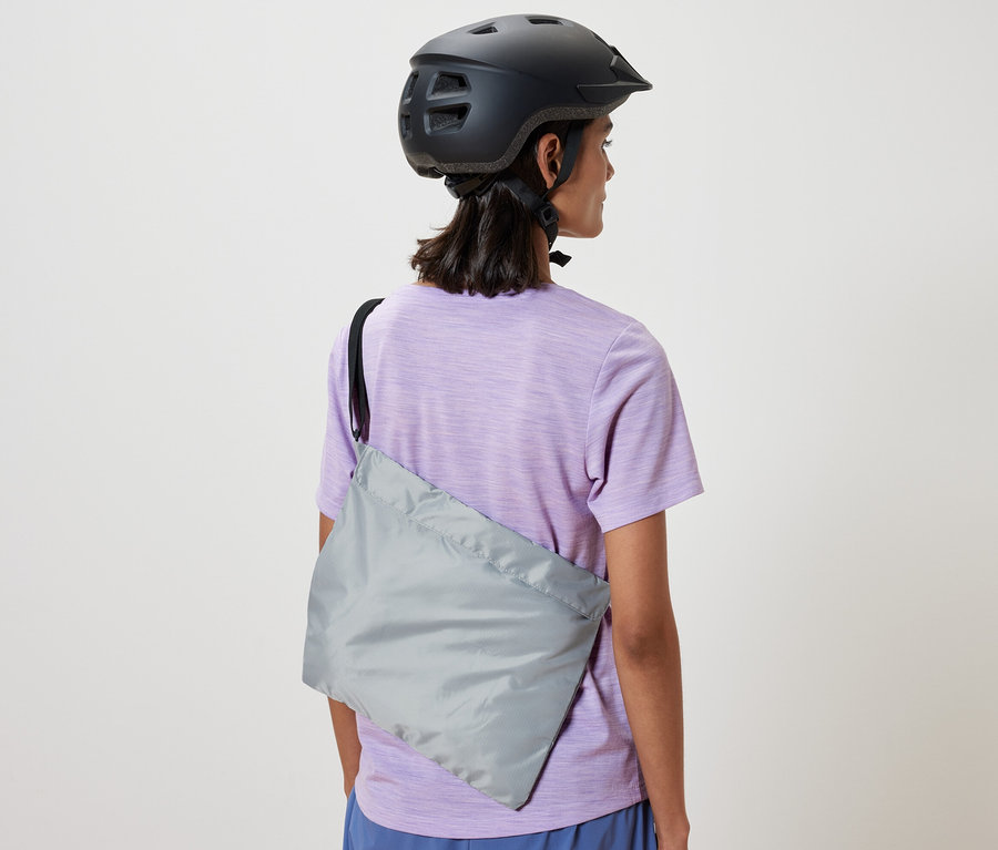 Žena s cyklistickou helmou má cez rameno prehodenú nákupnú tašku na bicykel.