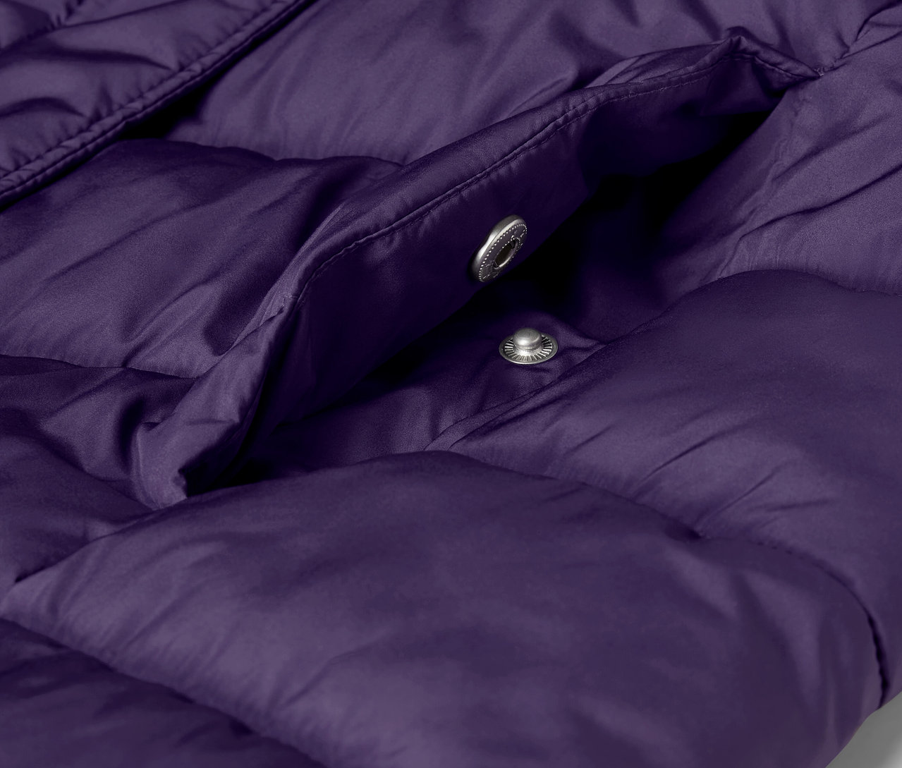 Detail fialovej prešívanej bundy s vreckom a striebornými patentkami.